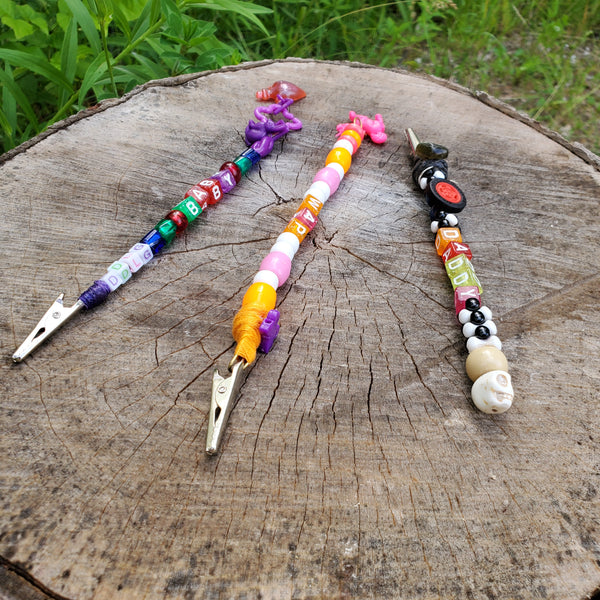 Three colorful beaded metal clips are arranged on a weathered tree stump outdoors, with green grass visible in the background.