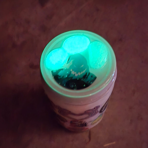 A small clear plastic cup topped with glowing green gems, photographed from above on a dark brown surface.