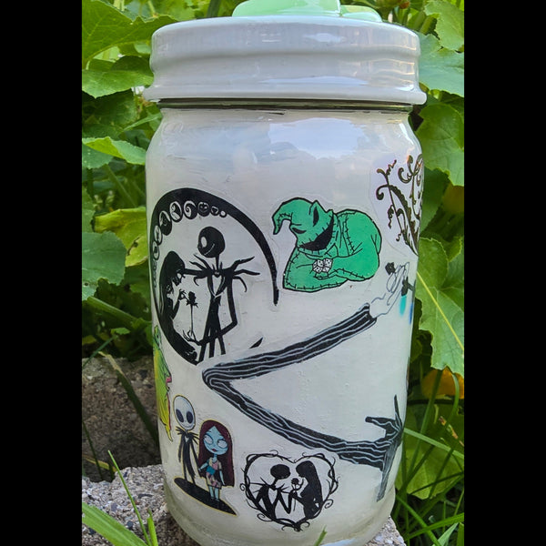 A white ceramic jar decorated with black and green Jack Skellington themed illustrations, photographed outdoors on a stone surface with green foliage in the background.